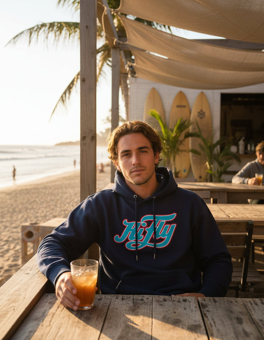 junger Mann in Strandbar, der einen dunkelblauen Hoodie trägt mit HiFly Logo in Hellblau und Rot.