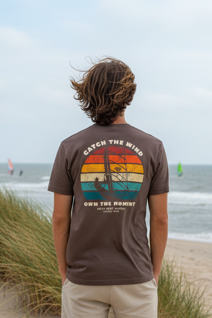 Junger Mann mit HiFly T-Shirt und Suferdesign auf dem Rücken steht in der FD<üne und blickt aufs Meer