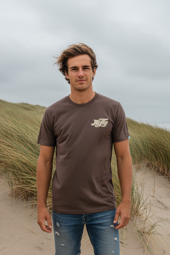 Junger Mann im Surferlook mit HiFly T-Shirt in Braun in den Dünen